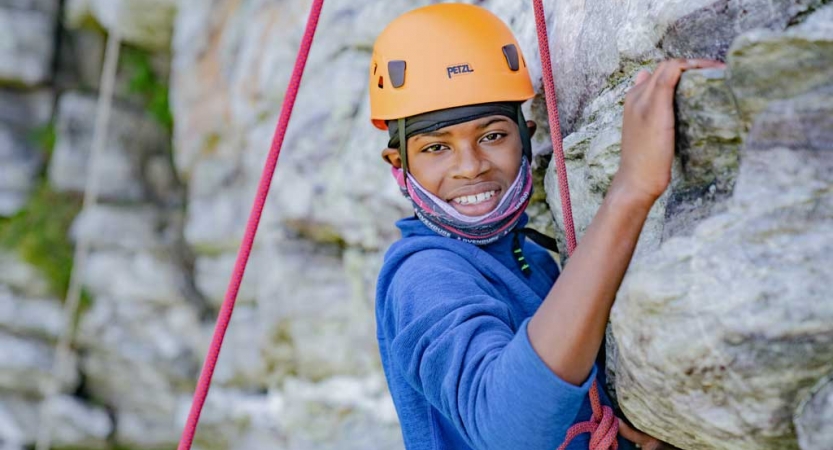 A person wearing safety gear is secured by ropes while rock climbing. They pause to smile for the photo. 